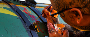 Steady hands guide a pinstriping brush, adding decorative flourishes to a custom smoker.