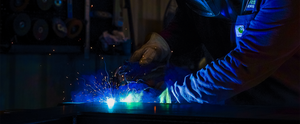 A skilled welder uses a torch to join metal components, creating a custom design. Sparks illuminate the workspace.